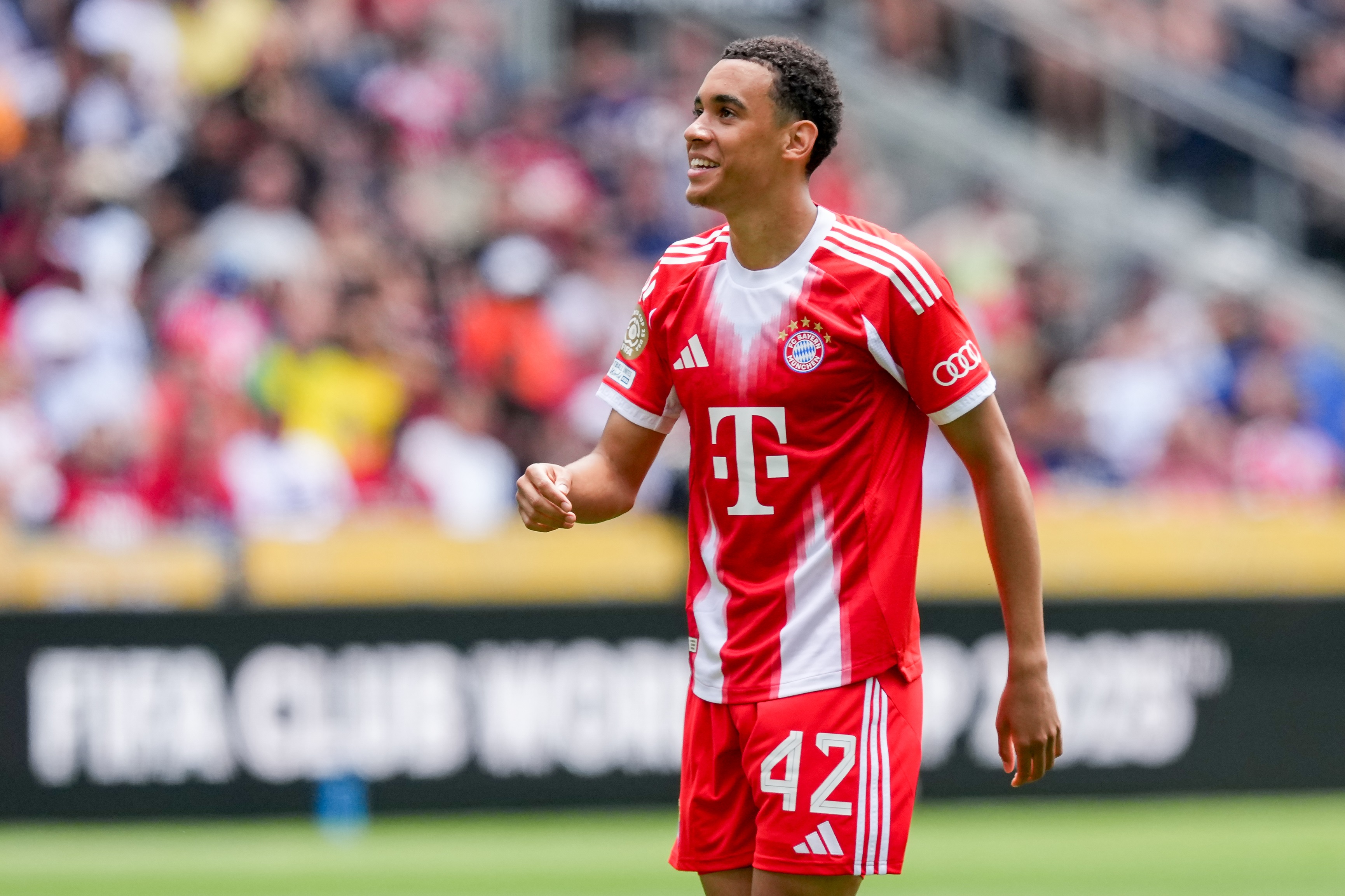 Jamal Musiala walks on the pitch with new Bayern home shirt.