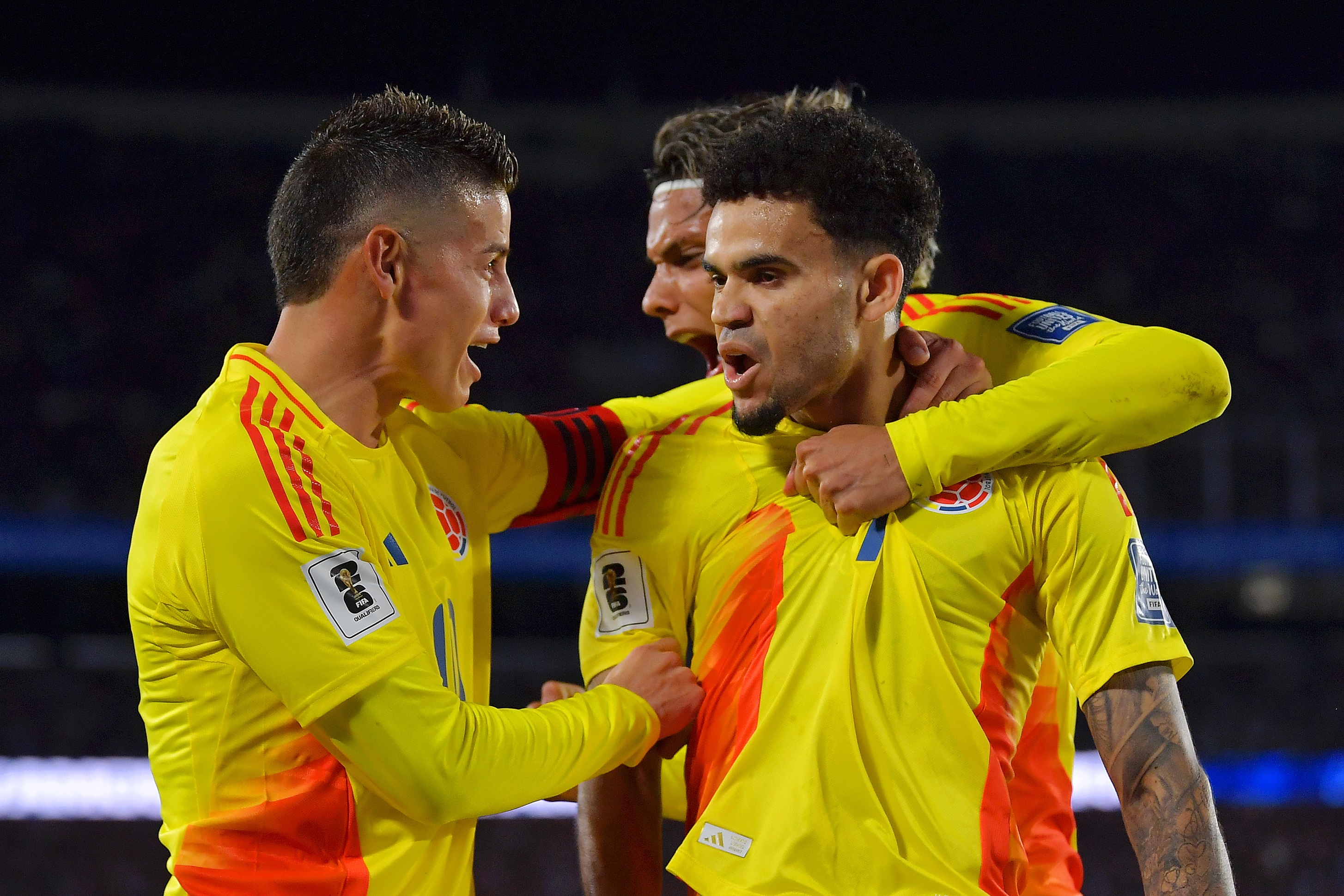 Luis Diaz is hugged by two Colombia teammates.