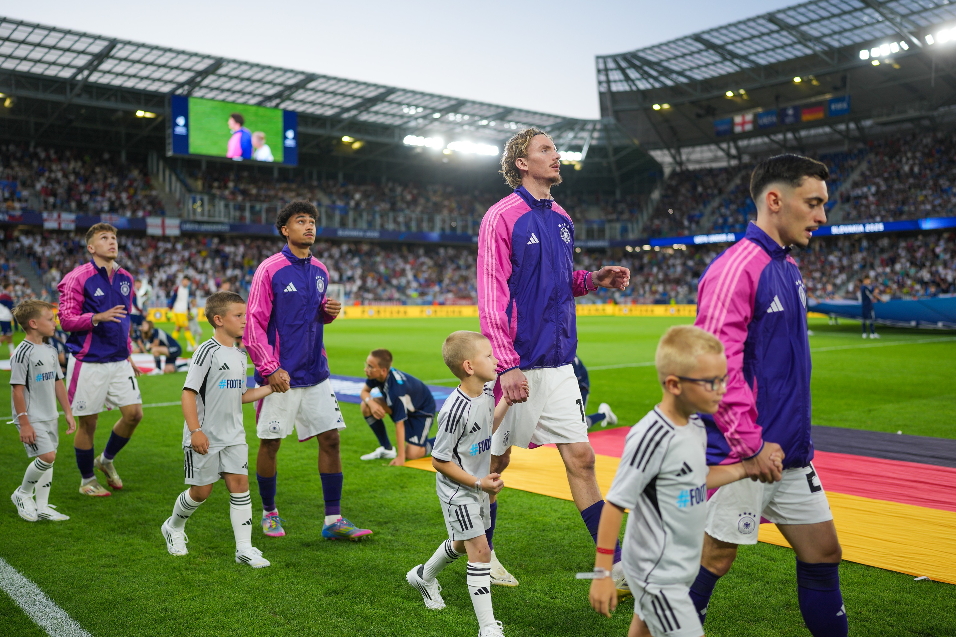 Nick Woltemade holds a mascot's hand as he walks on the pitch.