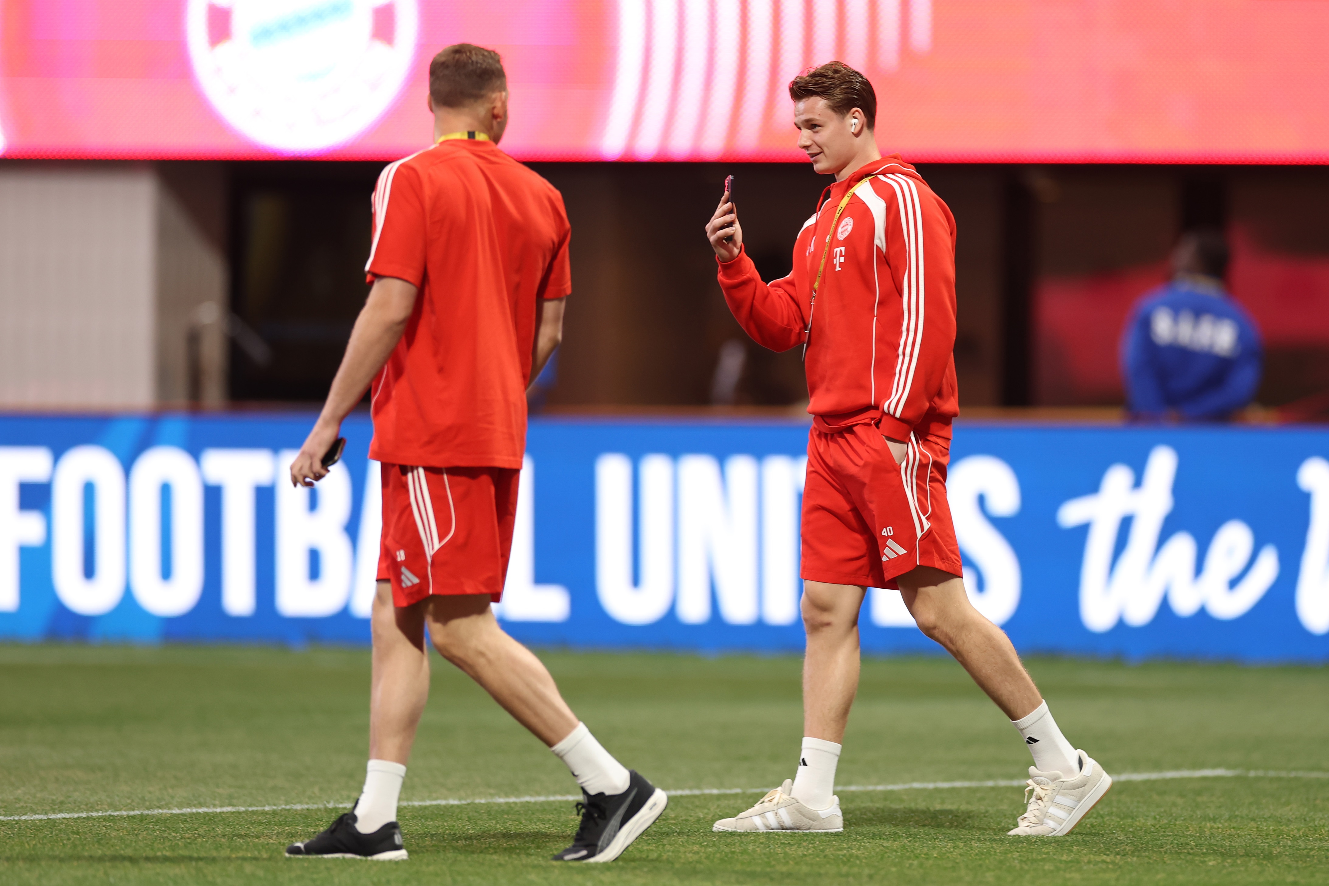 Jonas Urbig walks on the pitch with Daniel Peretz whilst holding his phone.