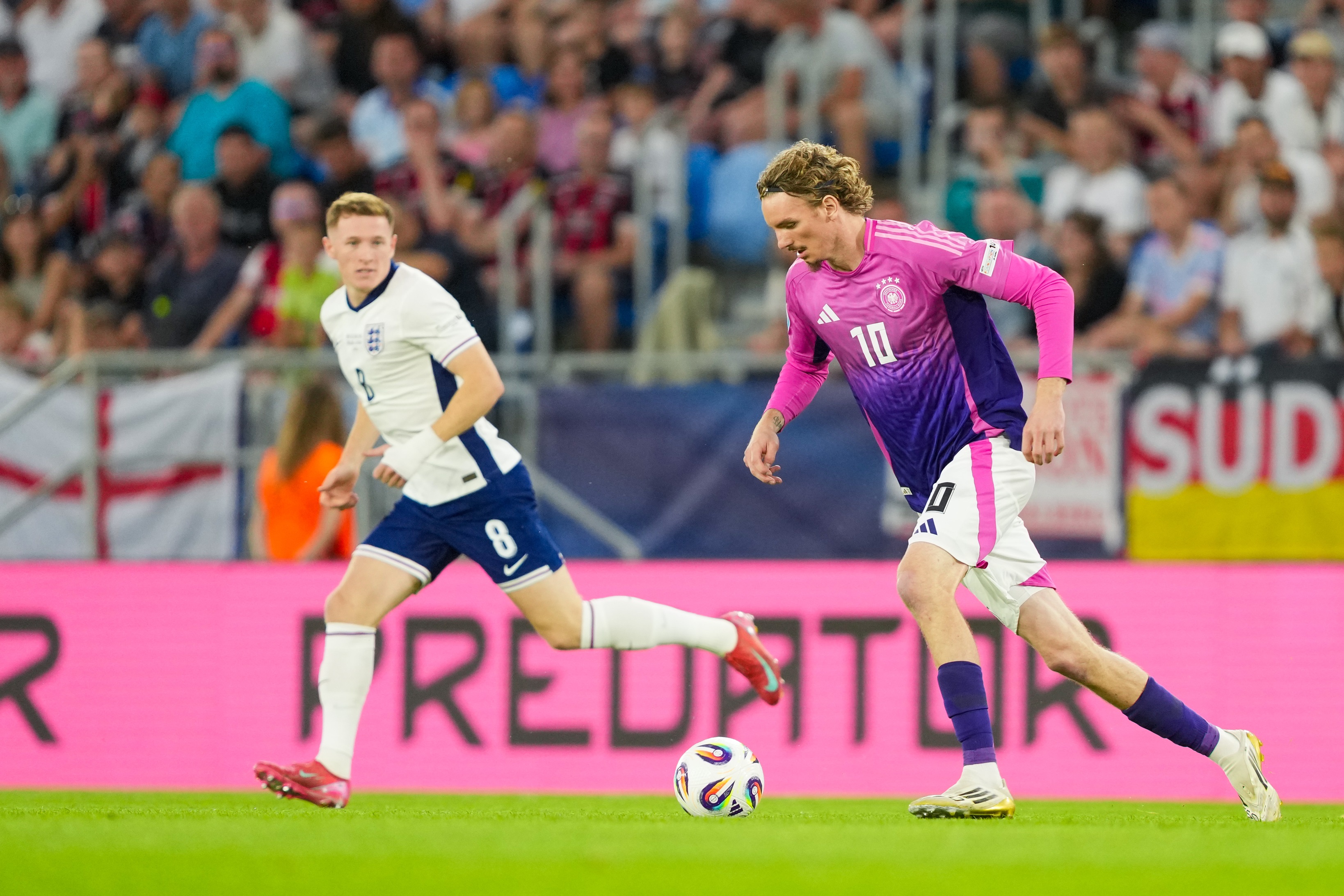 Nick Woltemade dribbles with the ball and is picture alongside an England player running.