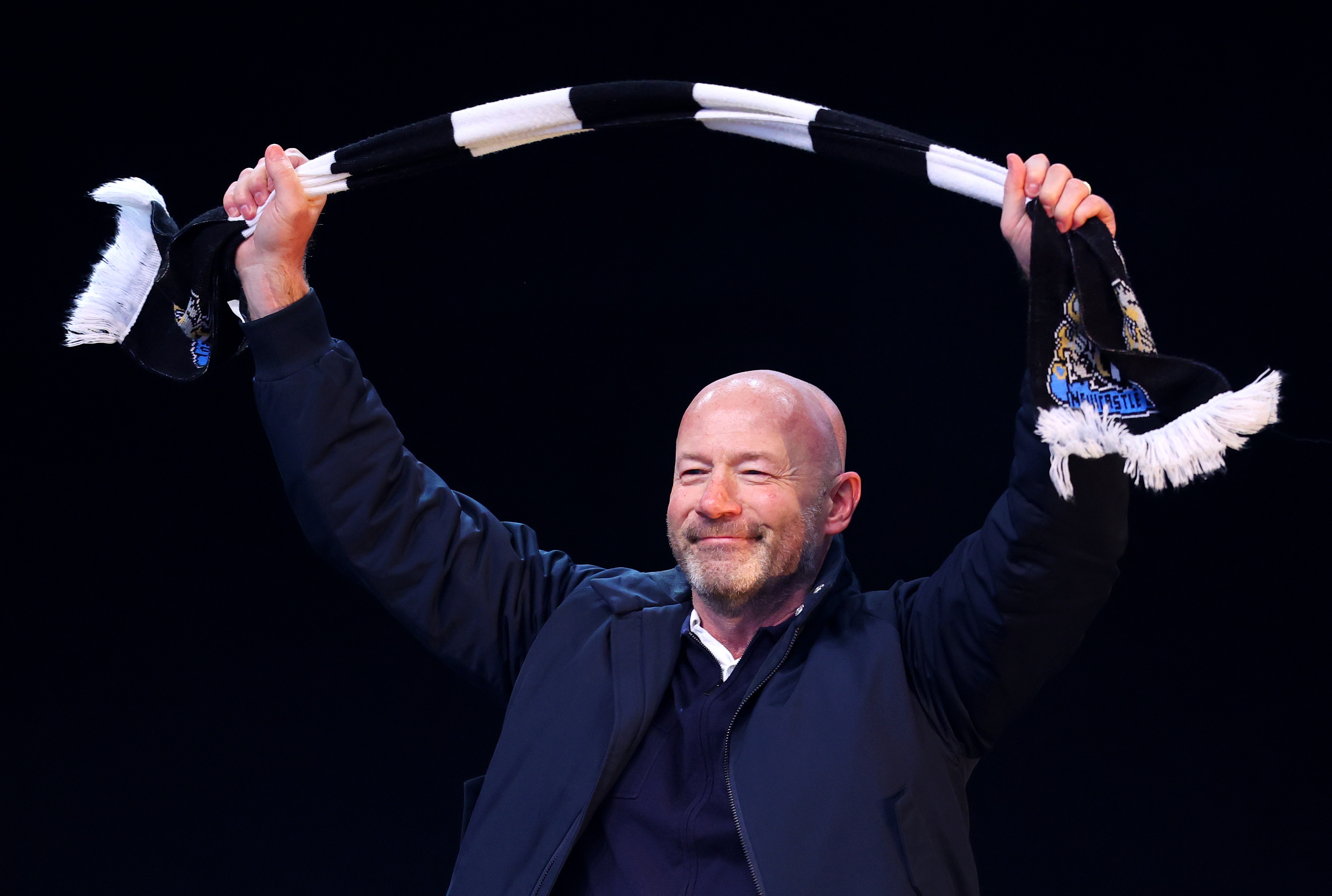 Alan Shearer holds up a black and white scarf.
