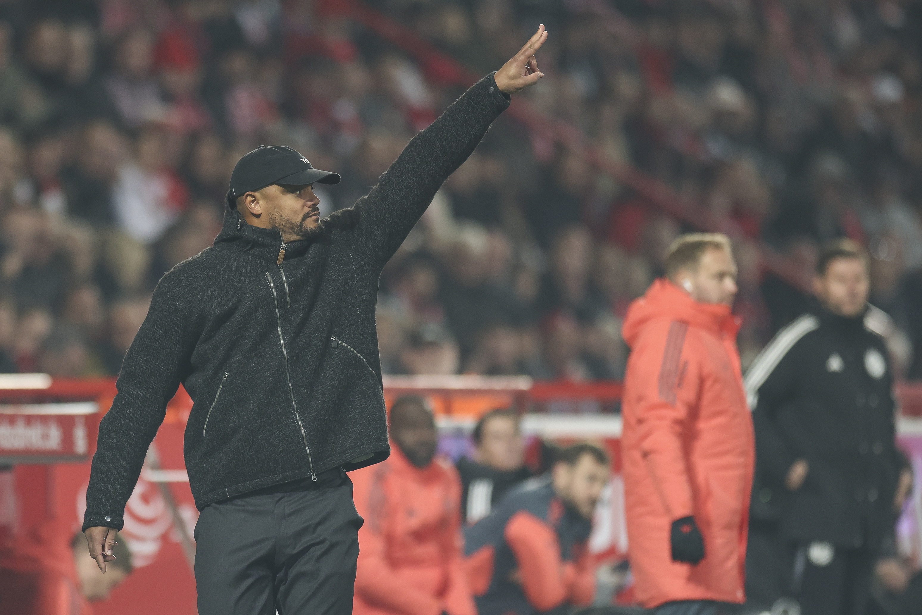 Vincent Kompany makes a hand gesture while standing on the touchline during Bayern game.