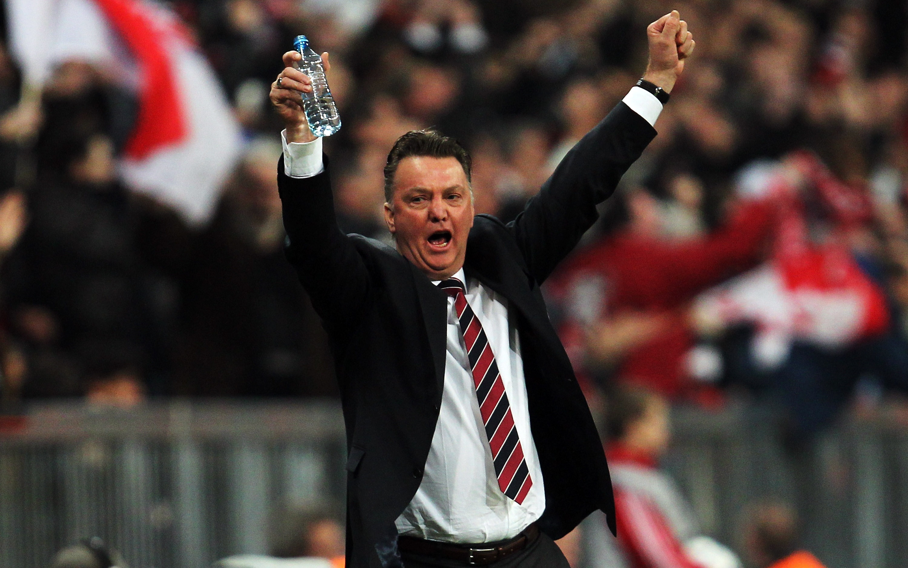 Louis van Gaal throws his arms up in the air in triumph.