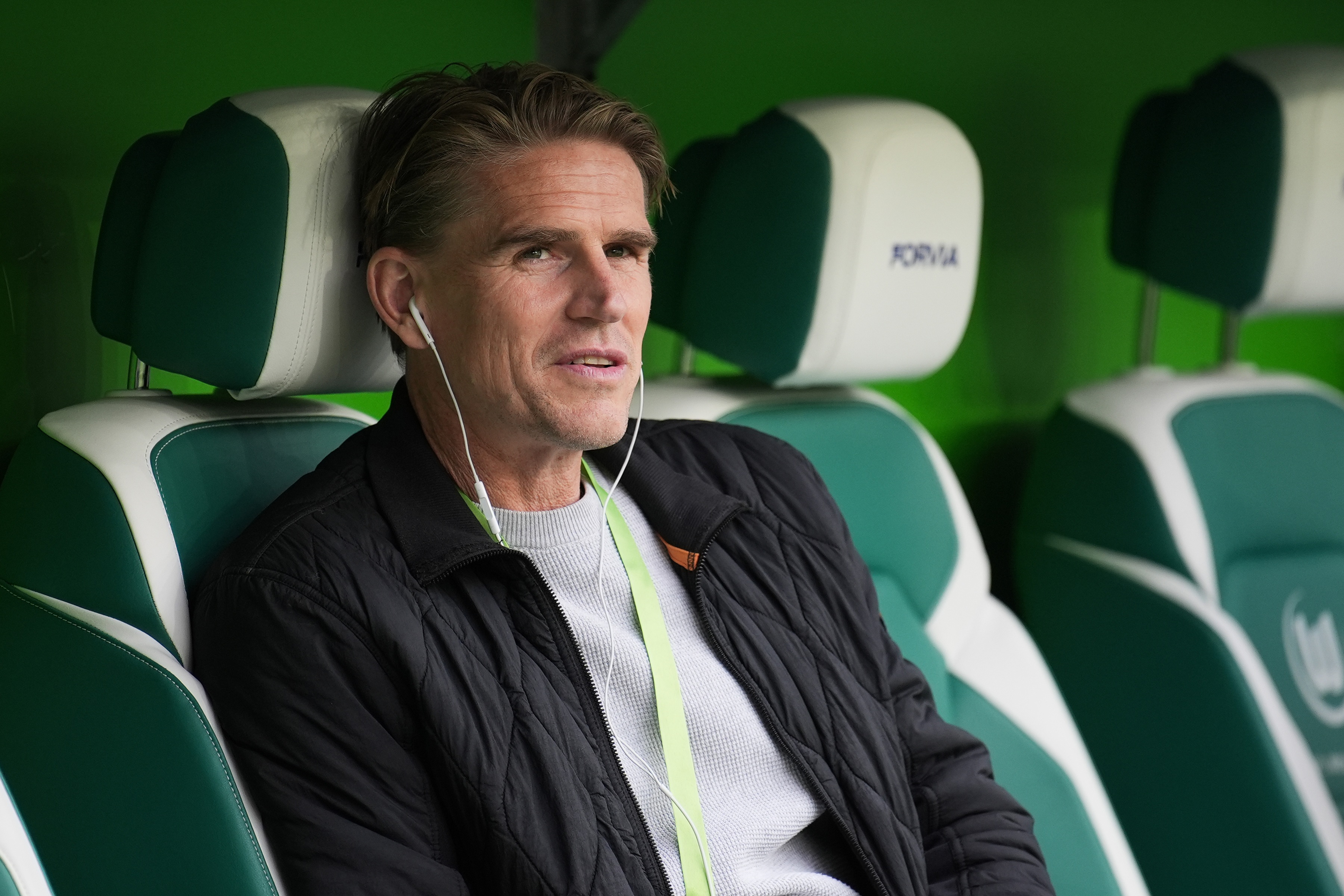 Bayern sporting director Christoph Freund sits in a green chair and listens to audio from his wire headphones.