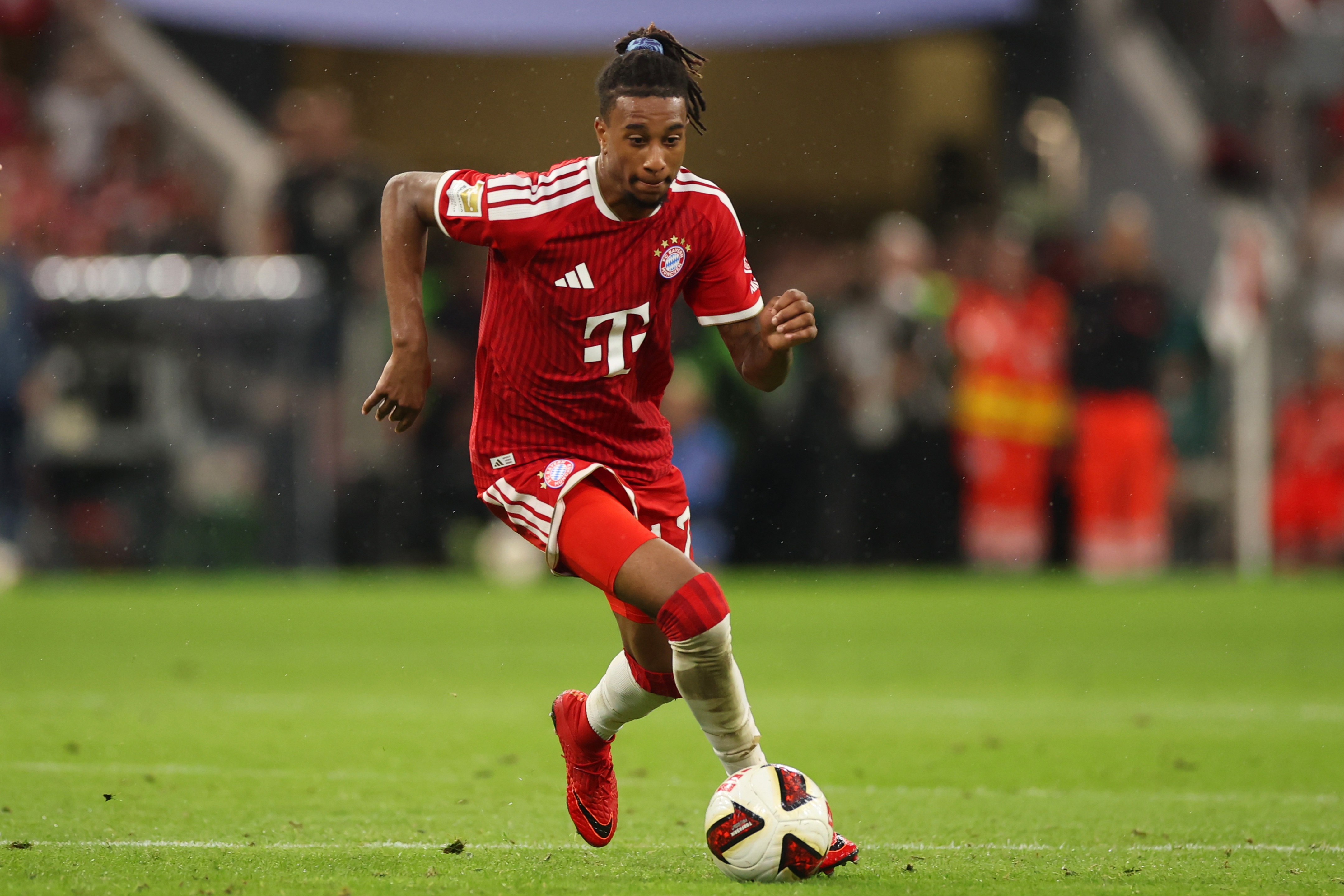 Michael Olise dribbles on the ball for Bayern Munich in a red kit.