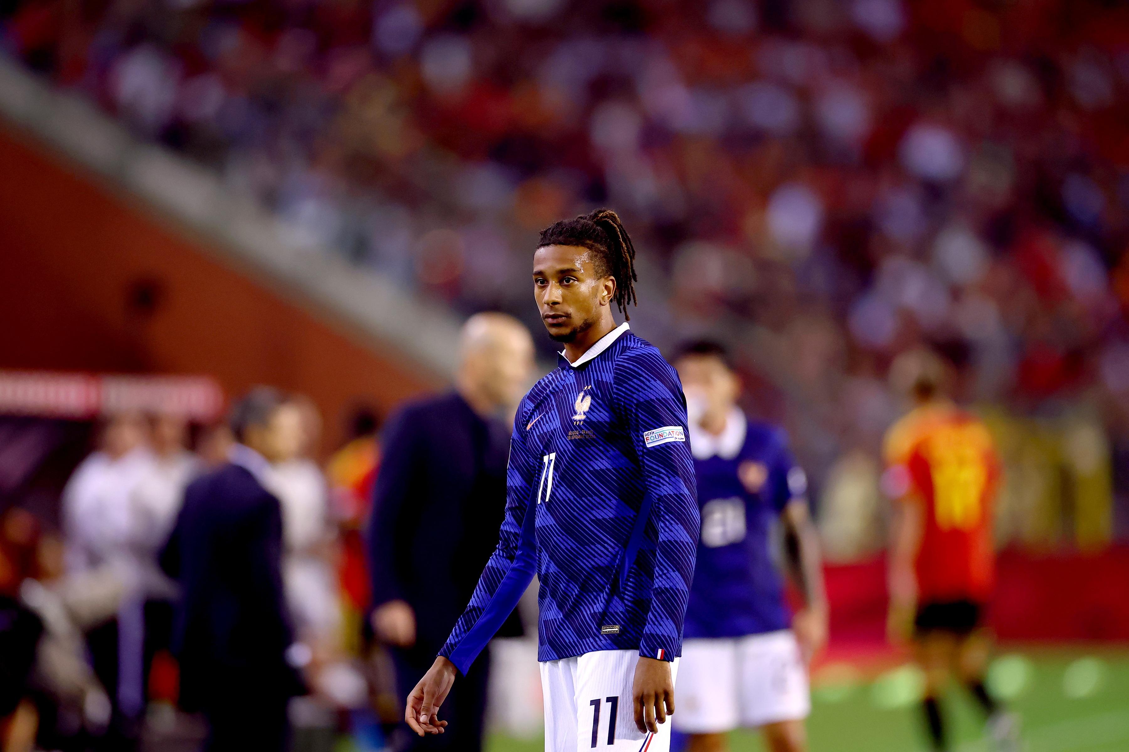 Michael Olise walks on the pitch wearing a blue France jersey.